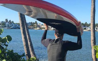 Man looking out on ocean near SeaGlass Jupiter Island with surf board balanced on his head