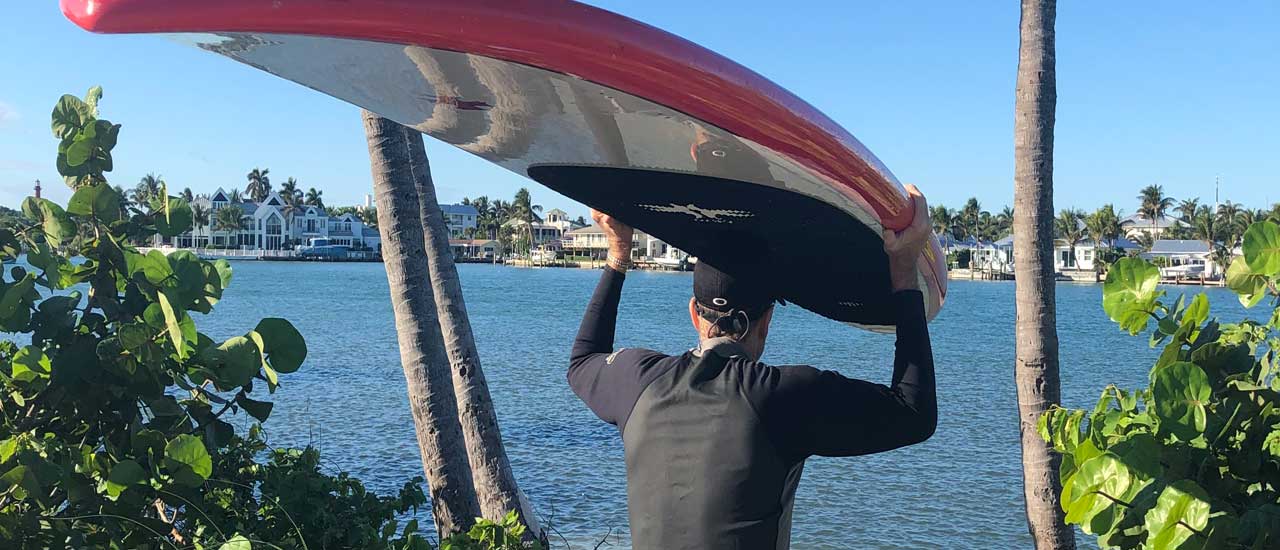 Man looking out on ocean near SeaGlass Jupiter Island with surf board balanced on his head